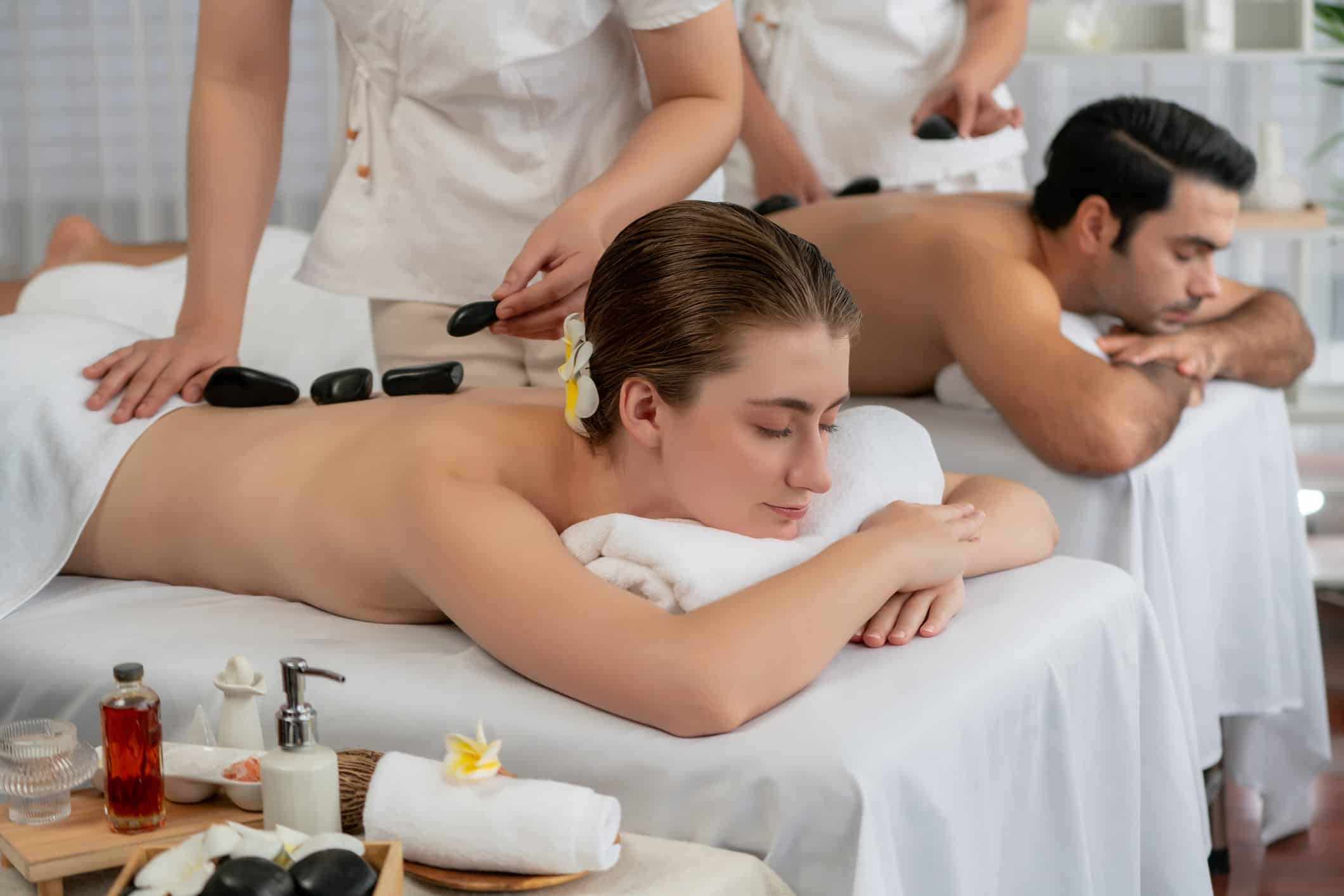 Hot stone massage at spa salon in luxury resort with day light serenity ambient, blissful couple customer enjoying spa basalt stone massage glide over body with soothing warmth. Quiescent