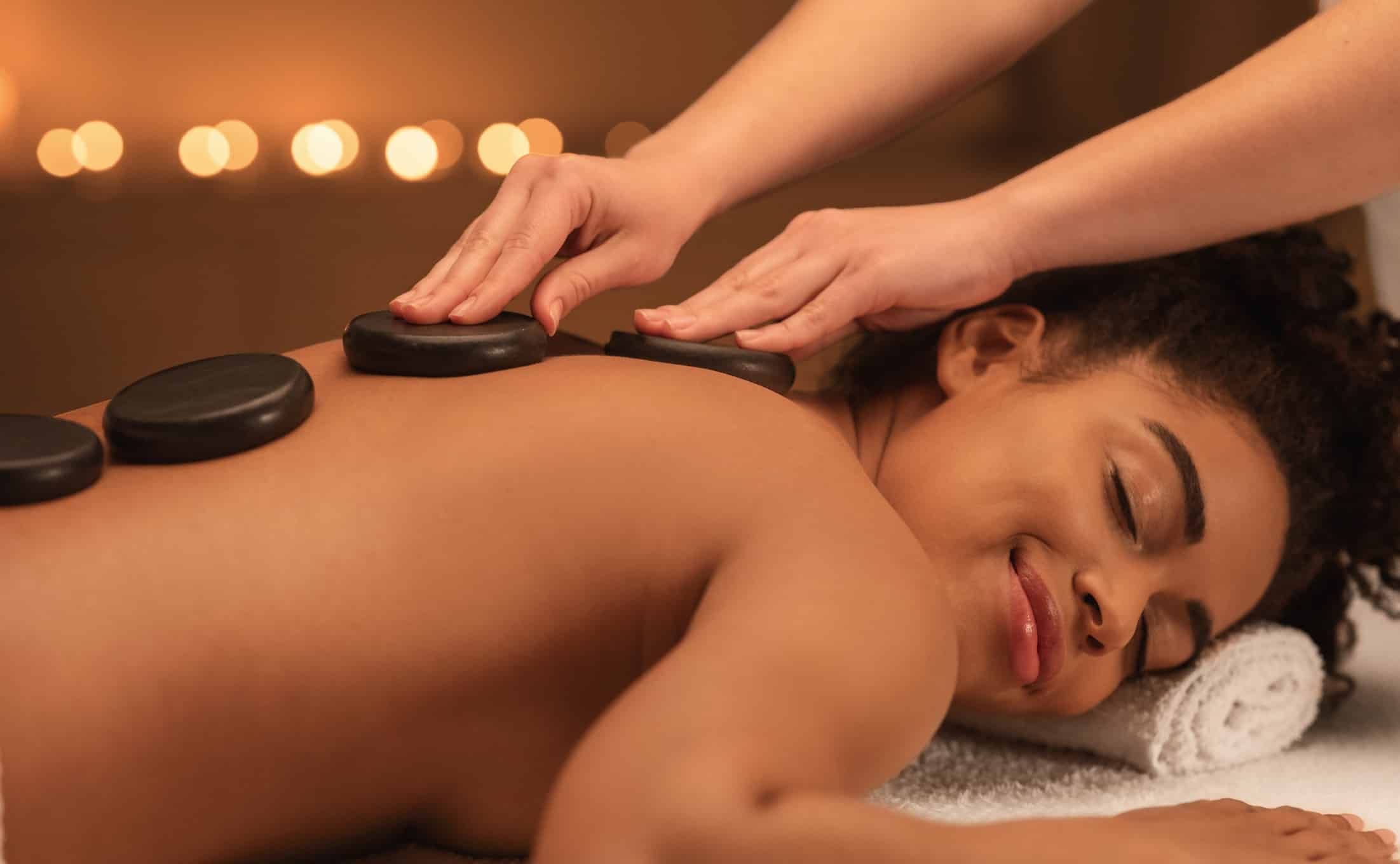 Healing hot stone massage for joyful black woman at luxury spa, closeup